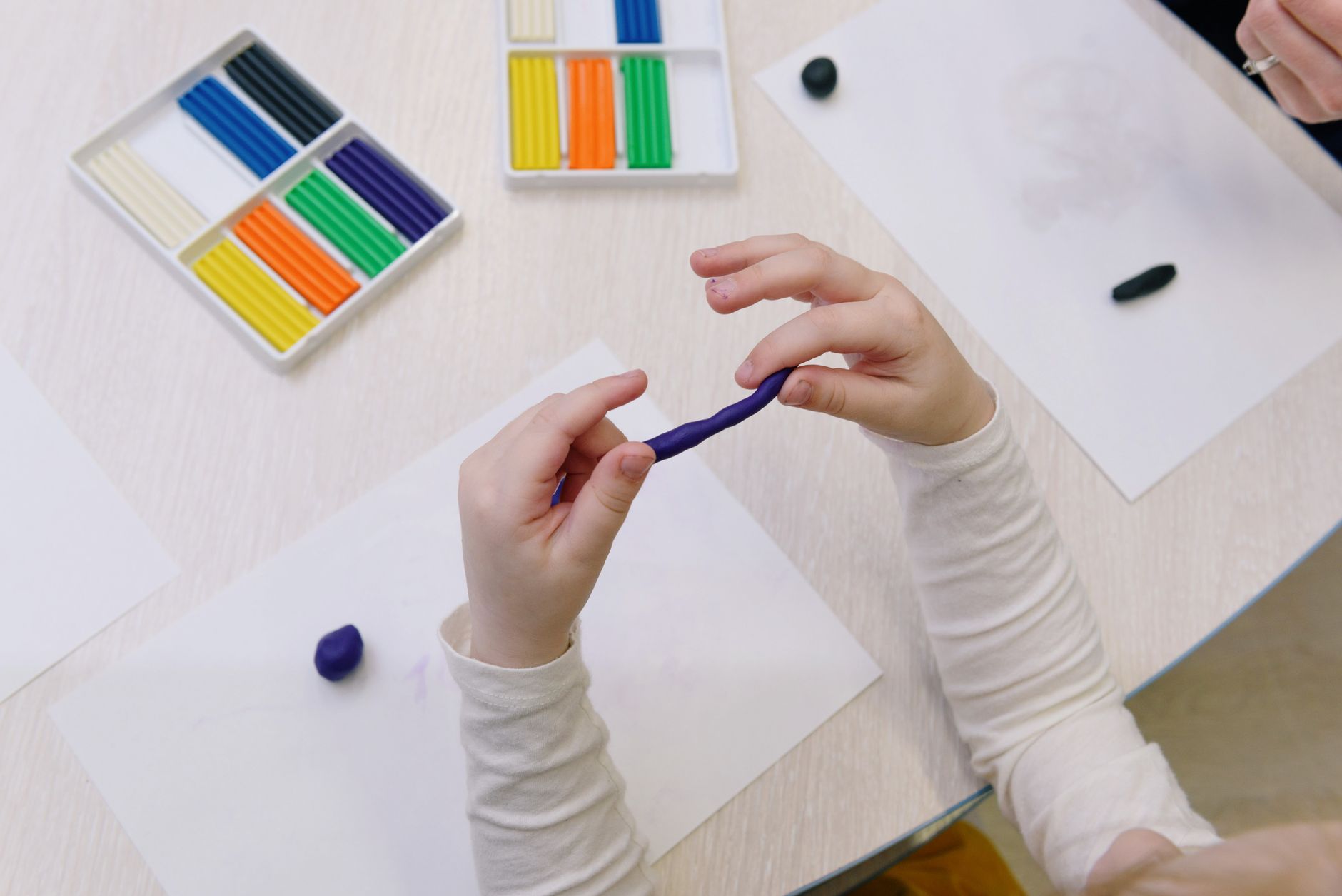 Overhead view of a child shaping purple modelling clay, surrounded by colorful clay sticks.